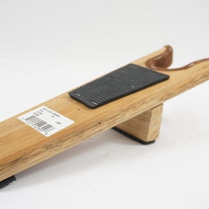 May include: A wooden boot jack with a natural light brown wood grain finish. The tool features a black rubber grip pad on the top surface and a U-shaped heel notch at the end. A white rectangular product label with a barcode is attached to the side.