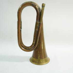 May include: A vintage brass bugle with a curved design. The bugle has a flared bell and a mouthpiece. The instrument is a warm brass color with some areas showing a darker patina. The bugle is likely an antique or a replica.