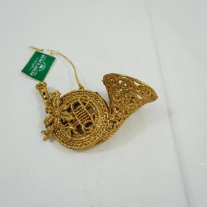 May include: Gold glitter Christmas ornament shaped like a French horn. The ornament has a delicate, intricate design.