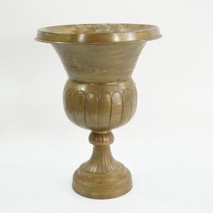Könnte beinhalten: Eine bronzefarbene Urne mit einem breiten, ausgestellten oberen Teil und einem bauchigen Mittelteil. Die Urne hat einen Sockel und ist mit vertikalen Rillen verziert. Das Gesamtdesign ist klassisch und dekorativ.