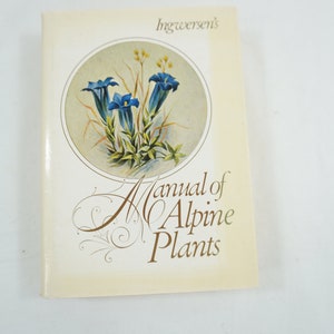 以下が含まれることがあります： インガーセンの「高山植物マニュアル」というタイトルのヴィンテージブック。表紙には、黄色い背景に青い花と白い花、緑の葉が描かれた円形のイラストが描かれている。