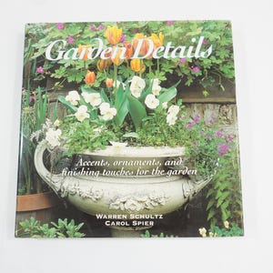以下が含まれることがあります： 「ガーデン・ディテール」というタイトルの書籍。白いプランターに花が植えられており、「アクセント、オーナメント、そして庭の仕上げ」というテキストが書かれている。