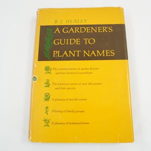 May include: A Gardener's Guide to Plant Names book by B.J. Healey. The yellow book has a brown band with the title and a green botanical illustration. The book's cover lists the common names of garden flowers and their botanical equivalents.