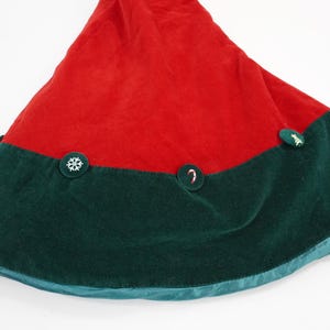May include: A conical Christmas tree skirt featuring a vibrant red upper section and a deep forest green border. The skirt is adorned with circular green fabric buttons, each displaying a unique white embroidered icon, including a snowflake and a candy cane.