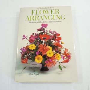 May include: A white ceramic mug with a black handle and the text "But First, Coffee" in a black, bold font. The mug is sitting on a wooden surface. The mug is 4 inches tall.