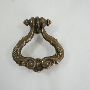 May include: Ornate brass door pull with a decorative design. The pull is shaped like a teardrop with a loop at the top.