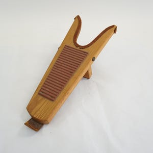 May include: Wooden boot jack with a light brown finish. The boot remover has a brown rubber insert and a notched design to help remove boots. The boot jack is made of wood and has a small support leg.