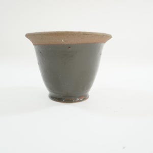May include: A small, gray ceramic pot with a brown rim. The pot is glazed and has a smooth finish.