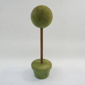 May include: A decorative topiary with a round, green sphere atop a brown stem, set in a matching green pot. The topiary is a simple, yet elegant, accent piece for home decor. The sphere has a textured surface.