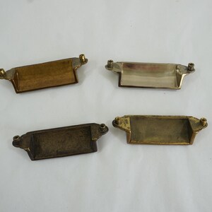 May include: Four antique brass drawer pulls with a rectangular shape and a slightly curved top. The pulls have a brushed finish and are in good condition.
