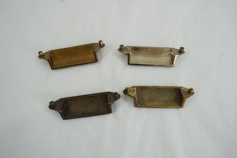 May include: Four antique brass drawer pulls with a rectangular shape and a slightly curved top. The pulls have a brushed finish and are in good condition.
