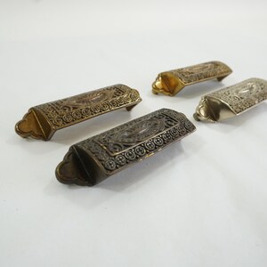 May include: Four ornate metal drawer pulls with an intricate design. The pulls are in different finishes: gold, silver, and black.