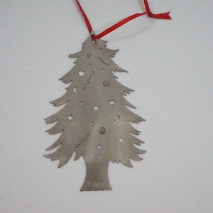 May include: A silver-colored Christmas tree ornament with decorative cutouts of stars, hearts, and swirls. The tree is suspended by a red ribbon. The ornament is made of metal and has a brushed finish.