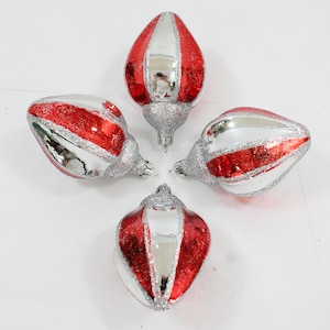 Puede incluir: Cuatro adornos navideños rojos y plateados con un diseño a rayas. Los adornos tienen forma de lágrima y un acabado brillante.