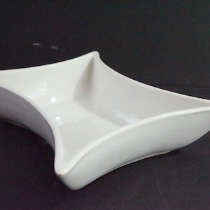 May include: A white ceramic serving dish with a unique, star-shaped design. The dish has two sections, perfect for serving snacks or appetizers.