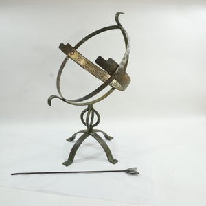 May include: An antique brass sundial with a curved armillary sphere design. The sundial has a base with three curved legs and a long pointer. The sundial has Roman numerals on the band.