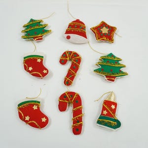 Op de afbeelding: Een verzameling kerstversieringen in verschillende vormen, waaronder kerstbomen, bellen, sterren, sokken, zuurstokken en kaarsen. De ornamenten zijn rood, groen en goudkleurig, met gouden ophangdraden.