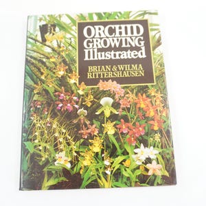 May include: A book titled "ORCHID GROWING Illustrated" with a cover featuring a vibrant array of orchids in various colors. The book's title is in a bold, serif font, with the authors' names below. The background is a lush, green garden setting.