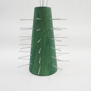 May include: A conical green wooden display stand featuring numerous thin, silver-coloured metal rods protruding horizontally from its surface. The structure has a flat base and a narrow top, with a smooth finish that reveals the natural wood grain.