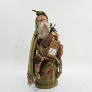 May include: A decorative figure of a bearded man wearing a green hooded cloak and carrying a bundle of items. The figure has a long white beard and is dressed in a plaid pattern. The figure is a Christmas decoration.
