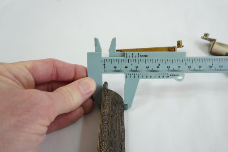 May include: A close-up of a metal decorative piece with intricate details. The piece is being measured with a caliper, showing a measurement of 6.8 cm.