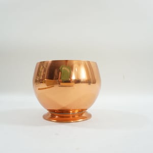 May include: A shiny copper planter with a rounded body and a flared base.