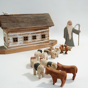 Puede incluir: Juego de madera del Arca de Noé con un arca estilo cabaña de troncos, una paloma, una figura de Noé y pares de animales. El arca es marrón con un techo desgastado. Los animales incluyen vacas, ovejas y pájaros.