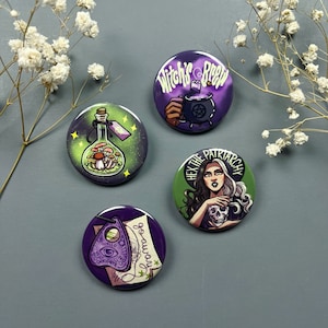 Puede incluir: Cuatro pines redondos con diferentes diseños. Un pin presenta una botella verde con champiñones, otro tiene un caldero de bruja, un tercero tiene una mujer con una calavera y el último tiene una tabla Ouija.
