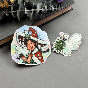 Könnte beinhalten: Zwei Aquarell-Aufkleber mit einem fantasievollen Weihnachtswichtel mit einer weißen Taube und einer Taube, die einen Mistelzweig trägt.