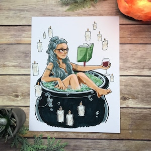 May include: A woman with blue hair and glasses relaxes in a cauldron filled with green liquid and bubbles. She is reading a book and holding a glass of red wine. Candles surround the cauldron.