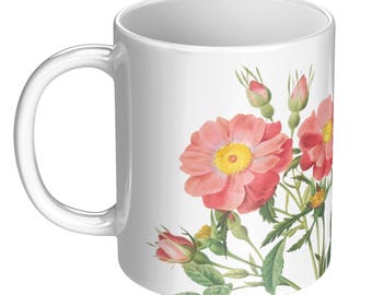 May include: White ceramic mug featuring a watercolor illustration of pink roses with yellow centers and green leaves. The floral design wraps around the mug, creating a decorative and artistic look. The mug has a curved handle.