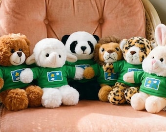 May include: A collection of plush animal toys, including a bear, lamb, panda, lion, leopard, and bunny, are seated on a pink upholstered chair. Each toy wears a green shirt with a blue and white emblem. The chair has a woven rattan frame.