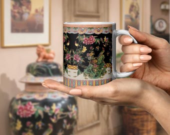 May include: A white ceramic mug with a silver handle, featuring a black background adorned with colorful floral and bird designs. The mug has a decorative border with a peach and gold trim.
