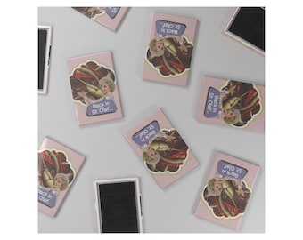 May include: A collection of pink rectangular magnets with a decorative image of a woman and food, with the text "Back in St. Olaf...". Several magnets are scattered across a light gray surface.