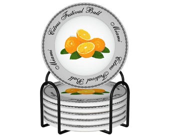 May include: A set of ceramic coasters with a black metal holder. Each coaster features a design of oranges and the text "Citrus Festival Ball Miami". The coasters are white with a gray border.