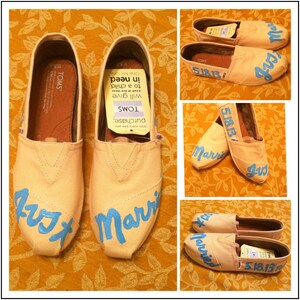 Könnte beinhalten: Ein Paar beigefarbene Canvas-Schuhe mit blauer Schrift. Die Schuhe sagen "Just Married" und "Married". Die Schuhe befinden sich auf einer gelben, floral gemusterten Oberfläche.
