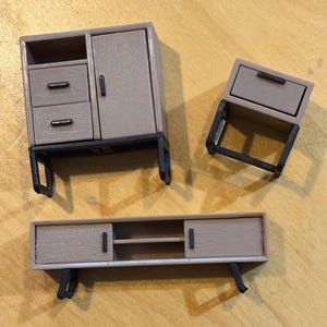 May include: Three miniature wooden furniture pieces with black metal legs. The pieces include a cabinet with two drawers and a door, a small side table with a drawer, and a long, low cabinet with two doors.
