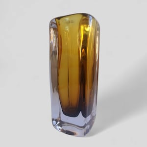 Könnte beinhalten: Eine hohe, bernsteinfarbene Glasvase mit einem einzigartigen, facettierten Design. Die Vase hat einen klaren Glasboden und eine leicht ausgestellte Öffnung.