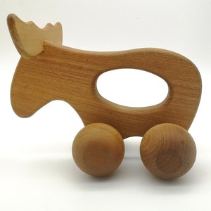 May include: A wooden toy moose with a handle and wheels. The moose is light brown and has a simple design.