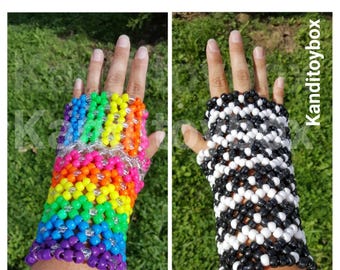 Puede incluir: Dos guantes sin dedos hechos de cuentas de plástico. Un guante presenta un patrón de arcoíris vibrante con filas horizontales de cuentas rojas, naranjas, amarillas, verdes, azules y moradas. El otro guante tiene un patrón de cuadros blanco y negro.