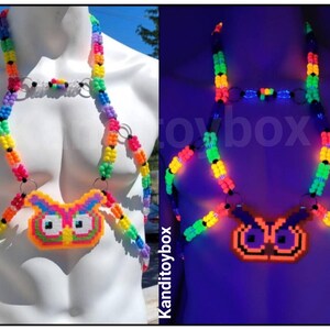 Peut inclure: Un harnais de corps compos&eacute; de perles en plastique multicolores dispos&eacute;es en arc-en-ciel, avec un pendentif central en forme de hibou. Le design inclut des anneaux m&eacute;talliques argent&eacute;s reliant les brins de perles qui brillent sous lumi&egrave;re UV.