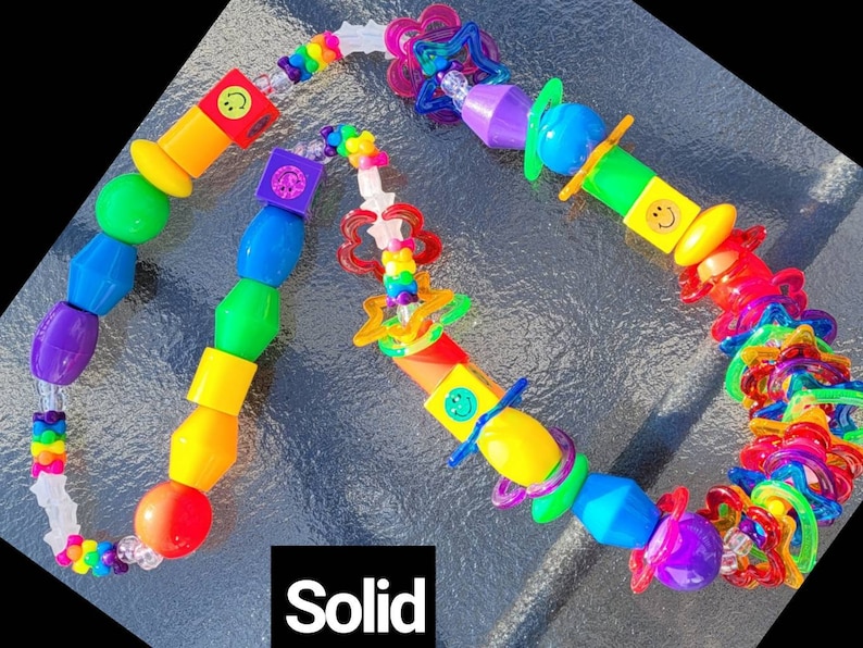 May include: A colorful beaded necklace with a variety of shapes and sizes. The beads are in a rainbow of colors, including red, orange, yellow, green, blue, and purple. Some beads have smiley faces. The word "Solid" is in the image.
