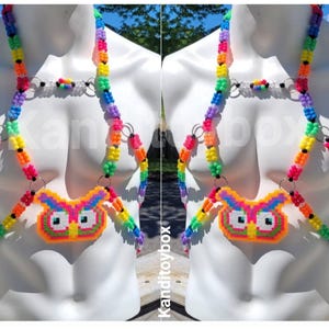 Peut inclure: Un harnais de corps compos&eacute; de perles en plastique multicolores dispos&eacute;es en motif arc-en-ciel. Le design comprend des anneaux m&eacute;talliques argent&eacute;s reliant les brins de perles et un pendentif central en forme de hibou fait de perles fusionn&eacute;es.