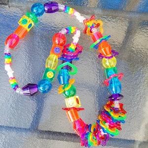 May include: A colorful necklace featuring a variety of plastic beads in shades of red, orange, yellow, green, blue, and purple. The necklace includes star, smiley face, and geometric shaped beads. The necklace is approximately 18 inches long.