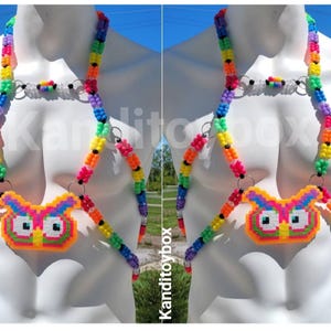 Peut inclure: Un harnais de corps compos&eacute; de perles en plastique multicolores dispos&eacute;es en arc-en-ciel, avec un pendentif central en forme de hibou fait de perles fusionn&eacute;es. Le design comprend des anneaux m&eacute;talliques argent&eacute;s reliant les brins de perles.