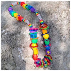 May include: A colorful necklace with a variety of plastic beads in rainbow hues. The necklace features a mix of shapes, including spheres, cubes, and rings, creating a playful and vibrant accessory.