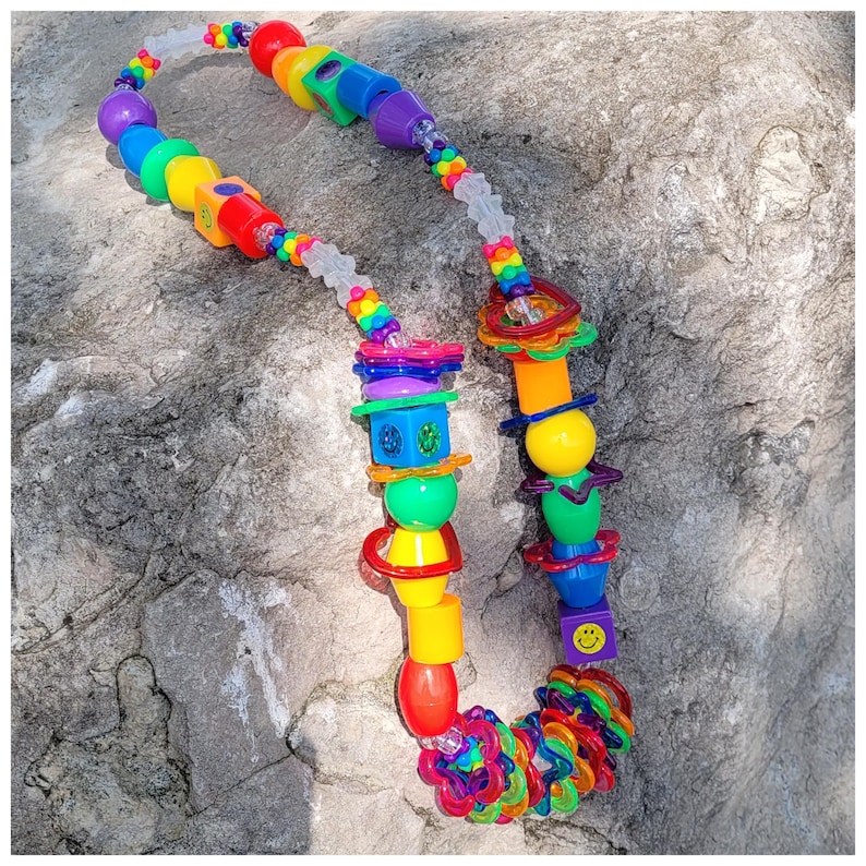 May include: A colorful necklace with a variety of plastic beads in rainbow hues. The necklace features a mix of shapes, including spheres, cubes, and rings, creating a playful and vibrant accessory.