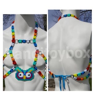 Peut inclure: Un harnais de corps en perles multicolores avec un pendentif central en forme de hibou pixelis&eacute; fait de perles en plastique. Le harnais est compos&eacute; de perles pony rouges, orange, jaunes, vertes, bleues et blanches reli&eacute;es par des anneaux en m&eacute;tal argent&eacute;.