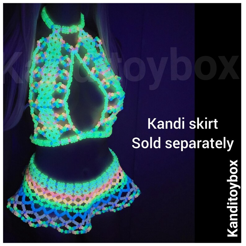 May include: A glow-in-the-dark beaded halter top and matching skirt set constructed from interconnected plastic beads. The garment features a lattice pattern that emits a bright neon green light in the dark. Text reads Kanditoybox and Kandi skirt Sold separately.