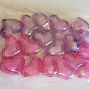 K&ouml;nnte beinhalten: Ein klarer Plastikbeutel gef&uuml;llt mit herzf&ouml;rmigen Perlen. Die Perlen sind rosa und lila mit schillerndem Glanz. Die Herzen sind unterschiedlich gro&szlig; und eng beieinander.